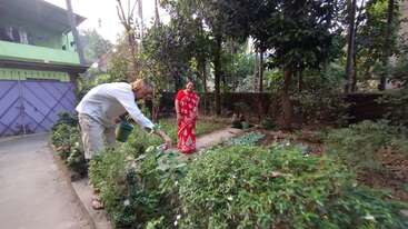 L'image montre une personne s'occupant d'un jardin, avec une grande étendue d'herbe et quelques arbres en arrière-plan, entourés d'une clôture ou d'une autre limite.