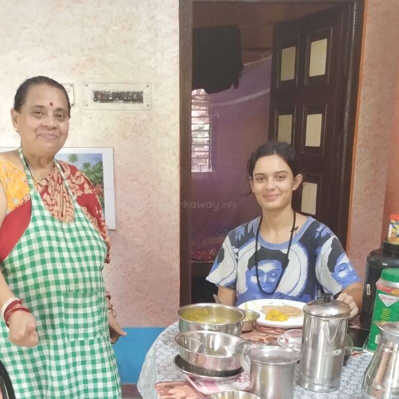 L'image représente deux femmes debout à côté d'une table chargée de vaisselle et d'ustensiles de cuisine, sur fond de porte et de mur.