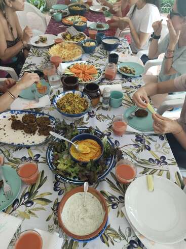 A group of people gather around a table filled with colorful dishes, dips, and drinks, enjoying a lively and communal vegetarian meal together.