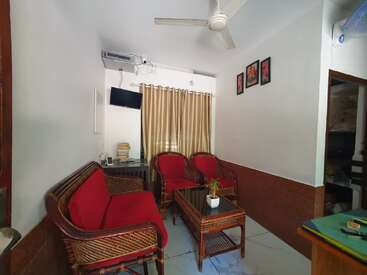 Dieses gemütliche Wohnzimmer hat Korbmöbel mit roten Kissen, einen kleinen Couchtisch, beige Vorhänge, einen Deckenventilator, Wandkunst, einen Fernseher und eine Klimaanlage.