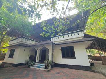 Dieses Bild zeigt ein charmantes weißes Haus mit einem Schrägdach, das von üppigen grünen Bäumen umgeben ist, mit gewölbten Türöffnungen, Topfpflanzen und schattigen Außenbereichen.