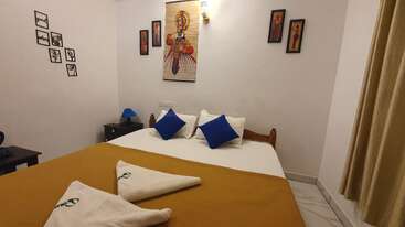 Dieses Bild zeigt ein gemütliches Schlafzimmer mit einem Holzbett, weißen Laken, blauen Kissen, einer gelben Decke, Wandkunst, Beistelltischen und einer warmen Beleuchtung, die eine einladende Atmosphäre schafft.