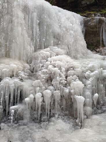 Uma cachoeira em cascata congelou completamente, formando camadas de gelo, pingentes de gelo e formações de gelo bulbosas. A cena brilha com texturas e detalhes gelados e intrincados de inverno.