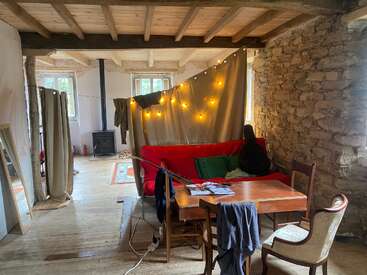 La imagen muestra un acogedor salón con un sofá rojo, una mesa de madera y una pared de piedra, que ofrece un ambiente cálido y acogedor con una iluminación suave y texturas naturales.
