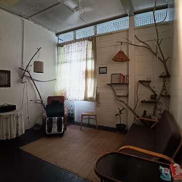 Um quarto aconchegante e minimalista, com galhos rústicos usados como decoração, móveis de madeira, uma cadeira de massagem, luz natural suave, estantes de livros e vasos de plantas, criando um ambiente relaxante.