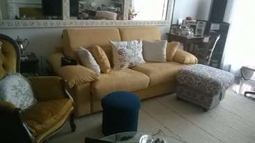 The image depicts a living room with a couch, coffee table, and other furniture, featuring a prominent rug and a large window, with a neutral color scheme and a minimalist aesthetic.