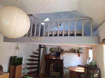 This cozy room features a loft bed accessed by a spiral staircase, paper lantern, wooden furniture, aquarium, bookshelves, and natural light from small windows.