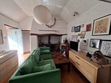 This cozy living room features a green sofa, wooden furniture, a fireplace with antlers above, wall art, a large paper lantern, and natural light.