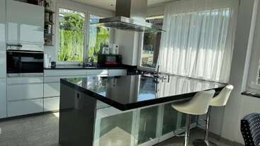 Essa cozinha moderna apresenta armários brancos brilhantes, uma ilha com bancada preta elegante, bancos de bar, janelas grandes com cortinas transparentes e eletrodomésticos de aço inoxidável, criando um espaço brilhante e contemporâneo.