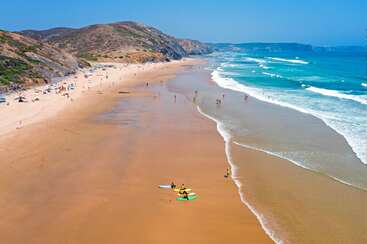 A imagem retrata uma cena serena de praia com mar calmo, areia branca e céu claro, com um grupo de pessoas aproveitando o ar livre em um dia ensolarado.