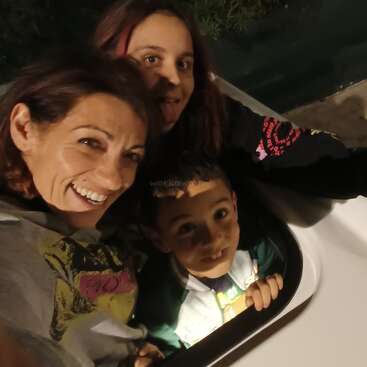 Trois personnes sourient et posent pour un selfie de nuit. Une femme adulte, une jeune fille qui fait une grimace et un garçon dans une aire de jeux.