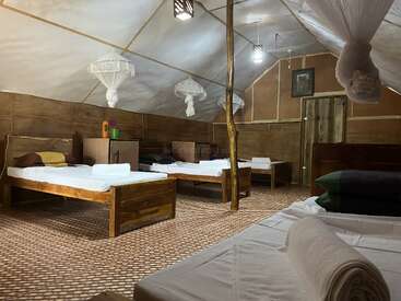 Cette image montre une chambre rustique de style dortoir avec des lits en bois, des draps blancs, des moustiquaires, un sol en bambou, un éclairage simple et une atmosphère confortable et organisée pour les séjours en groupe.