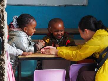 Three children and an adult sit at a table, laughing and playing together. The atmosphere is joyful, warm, and engaging, fostering connection and happiness.