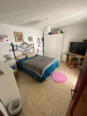 Dieses gemütliche Schlafzimmer hat ein dekoratives Kopfteil aus Metall, ein ordentlich gemachtes Bett, einen weißen Kleiderschrank, einen großen Fernseher, Kunstwerke an den Wänden, einen kleinen rosa Teppich und einen gefliesten Boden.
