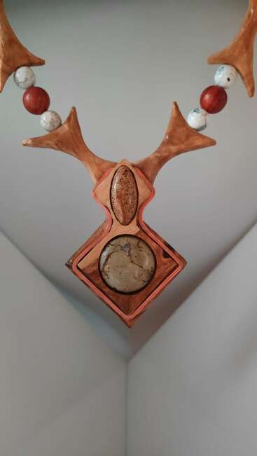 Dieses Bild zeigt ein dekoratives Objekt, das einem stilisierten Tierkopf mit Geweih ähnelt, mit Steinperlen und geometrischen Formen, in Erdtönen und mit aufwändiger Handwerkskunst.