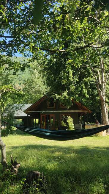 A cozy cabin nestled among lush green trees, with a hammock strung between trunks, dappled sunlight, and peaceful, grassy surroundings creating a serene retreat.