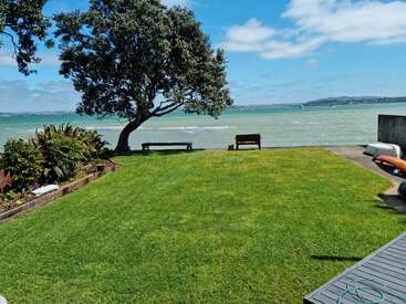 La imagen representa una serena zona de césped con un árbol, un banco y vistas al mar, evocando una sensación de tranquilidad y relajación en un pintoresco entorno al aire libre.