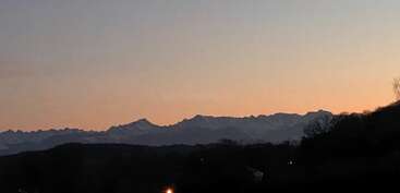 The image shows a serene mountain range at dusk, silhouetted against a soft orange and blue sky. Distant peaks are dusted with snow, creating a peaceful atmosphere.