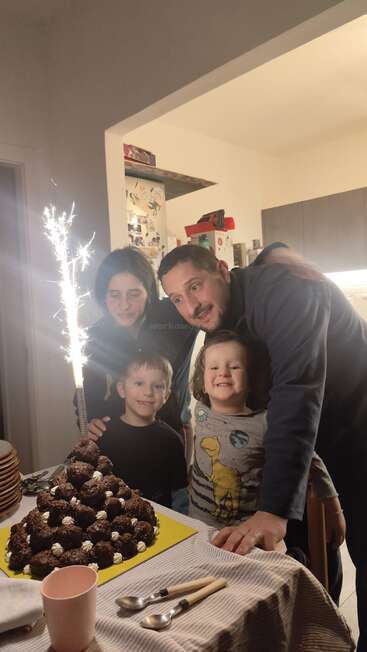 A family of four smiles around a pyramid-shaped dessert with sparklers. The children look excited, and the parents are joyful, celebrating a special occasion together.