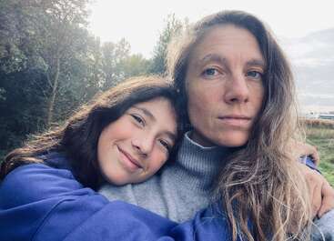 Das Bild zeigt eine Frau und ein Mädchen, die für ein Selfie im Freien posieren, wobei das Mädchen ihren Kopf auf der Schulter der Frau ruht.