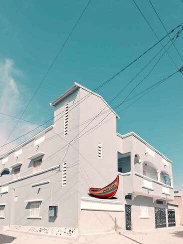 The image depicts a white building with a boat on the roof, featuring a blue sky with power lines and wires in the background.