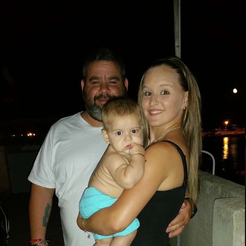 The image depicts a family of three posing for a photo at night, with a body of water and a full moon visible in the background.