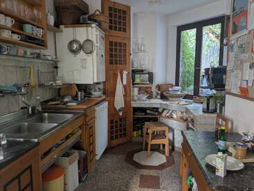 Essa cozinha aconchegante tem armários de madeira, uma pia dupla, prateleiras abertas com copos, um micro-ondas, uma pequena mesa com banquetas, janelas grandes e muita luz natural.