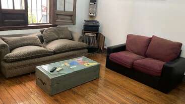 Ce salon confortable est composé de deux canapés, d'un coffre ancien en guise de table basse, de parquet, d'une fenêtre et d'étagères contenant une chaîne stéréo et des disques.