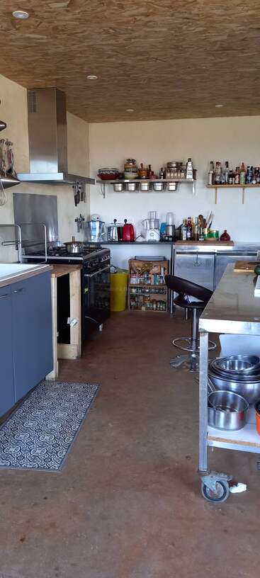 This image shows a modern kitchen with open shelves, utensils, spices, appliances, a stove, metal countertop, stools, bottles, and neatly organized cooking essentials.