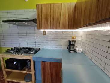 This image shows a modern kitchen with a blue countertop, wooden cabinets, a gas stove, coffee maker, blender, microwave, and white tiled backsplash with horizontal lines.