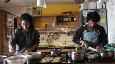 Eine Frau und ein Mann kochen zusammen in einer gemütlichen Küche. Sie bereiten das Essen zu, umgeben von Töpfen, Pfannen und Geschirr, und konzentrieren sich auf ihre Aufgaben.