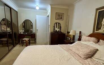 Este quarto tem uma cama grande com roupa de cama rosa, guarda-roupas com espelho, cômodas de estilo vintage, um abajur, quadros emoldurados e um ambiente tranquilo e aconchegante.