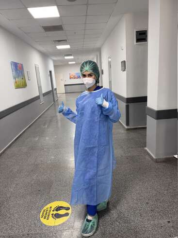 Un profesional sanitario, equipado con todo el equipo de protección individual —máscara, bata, guantes y gorro—, se encuentra en el pasillo de un hospital y levanta los dos pulgares en señal de aprobación.