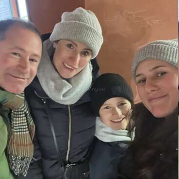 Un alegre grupo de cuatro personas, abrigadas con ropa de invierno, incluyendo gorros, bufandas y chaquetas, sonriendo y disfrutando de su tiempo juntos en el interior. Ambiente acogedor.