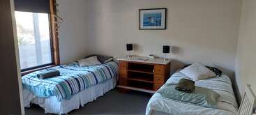 Esse quarto aconchegante tem duas camas de solteiro com roupa de cama listrada, uma cômoda com duas luminárias, uma janela grande e um quadro pendurado em uma parede branca.