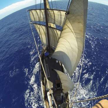 The image depicts a sailboat navigating through the ocean, with its sails unfurled and billowing in the wind, set against a backdrop of deep blue water.