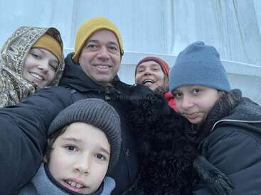 Eine fröhliche Gruppe von fünf Leuten, dick in Winterkleidung eingemummt, posiert eng beieinander für ein Selfie im Freien und lächelt trotz der kühlen Luft herzlich.