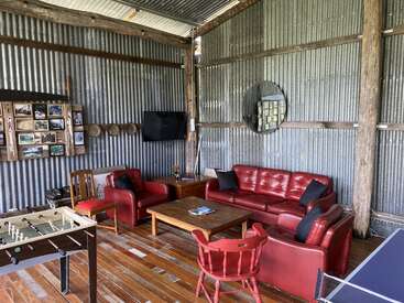 This cozy room features red leather sofas, a wooden coffee table, a foosball table, corrugated metal walls, rustic decor, and a wall-mounted TV. Relaxed atmosphere.