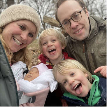 Das Bild zeigt eine fünfköpfige Familie, die für ein Foto posiert: zwei Erwachsene und drei Kinder, alle in Winterkleidung, an einem kalten Tag im Freien.