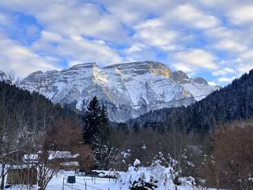 L'image représente un paysage hivernal serein avec une montagne enneigée, des arbres et un ciel bleu avec des nuages, évoquant un sentiment de tranquillité et de beauté naturelle.