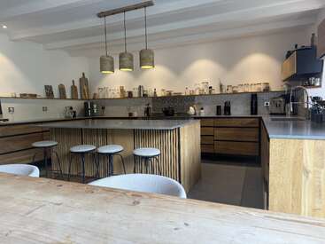 Essa cozinha moderna tem armários de madeira, uma ilha central com bancos altos, luminárias pendentes, prateleiras abertas com potes e uma mesa de jantar aconchegante na frente.