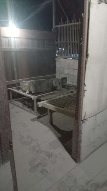 This image shows a dimly lit, dusty room with simple wire-frame beds, a box, concrete walls, and visible footprints on the dusty floor.