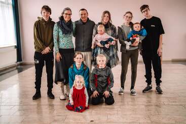 Un groupe de onze personnes, composé d'adultes, d'adolescents et de jeunes enfants, se tient debout et s'agenouille à l'intérieur sur un sol carrelé, souriant et posant pour une photo.