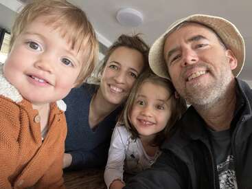 Eine glückliche vierköpfige Familie posiert eng beieinander und lächelt strahlend in die Kamera. Die gemütliche Umgebung im Haus verleiht dem Foto eine warme, fröhliche und liebevolle Atmosphäre.