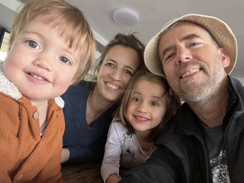 Una feliz familia de cuatro miembros posa muy unida, sonriendo alegremente a la cámara. El acogedor ambiente interior da a la foto una atmósfera cálida, alegre y cariñosa.