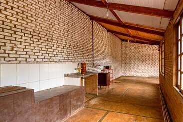 Cette image montre une cuisine spacieuse et rustique avec des murs en briques apparentes, des poutres en bois, de grandes fenêtres, un petit évier, des appareils électroménagers de base et une cuisinière en béton.