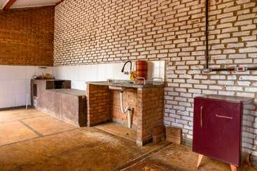 Cette cuisine rustique se caractérise par des murs en briques apparentes, un comptoir d'évier en briques, un petit réfrigérateur bordeaux, des surfaces carrelées, des étagères ouvertes, des meubles simples et un sol en béton. Un design confortable et minimaliste.