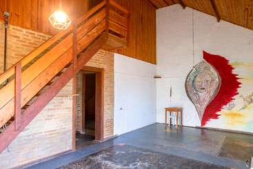 Cette pièce rustique et artistique se caractérise par des escaliers en bois, des murs en briques et en bois, une lampe suspendue géométrique et une grande peinture murale représentant un visage sur un mur blanc.