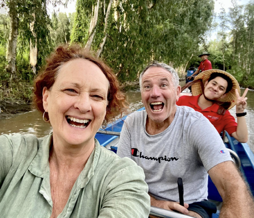 Three joyful people take a selfie while riding a boat on a river surrounded by lush greenery. They smile brightly, enjoying a fun and adventurous outing.