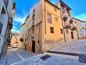 Une ruelle pittoresque bordée de charmants bâtiments en pierre et en stuc, avec des balcons en fer forgé et des façades rustiques, sous un ciel d'un bleu éclatant, dans une petite ville pleine de charme.